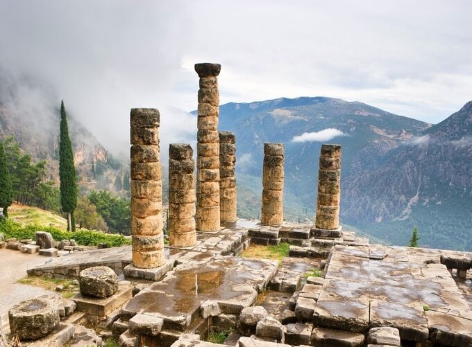 Ancient ruins of Delphi surrounded by mountains and greenery under a clear sky.
