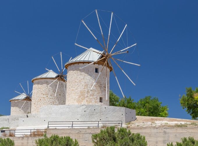 Alacatı windmills with stone walls and scenic town backdrop.