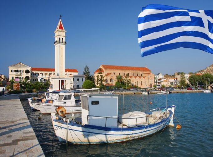 A charming Zakynthos seaside town lined with cozy homes and a waving Greek flag, capturing warm coastal life and island beauty.