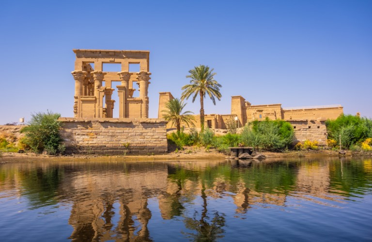 Ancient columned ruins in Aswan surrounded by natural scenery, capturing a peaceful atmosphere just before a scenic Nile cruise experience.