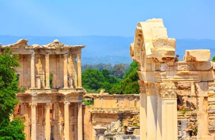 The Library of Ephesus stands amid spring nature, with a castle-like backdrop and lush surroundings highlighting this iconic ancient landmark.