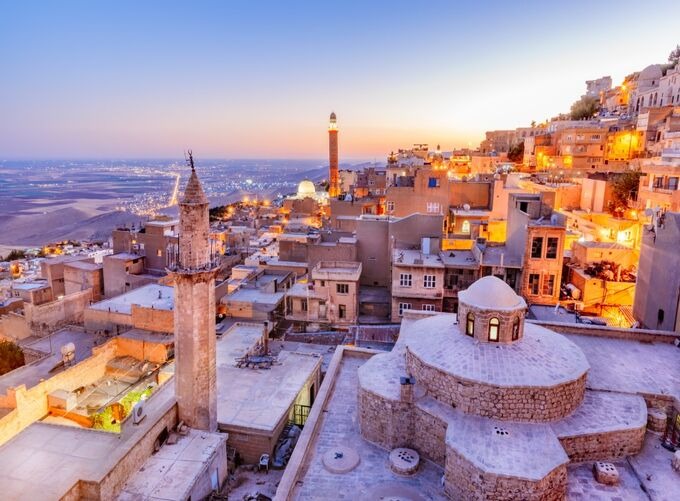 Panoramic view of Mardin with historic stone buildings, minarets and wide Mesopotamian plains stretching into the horizon.