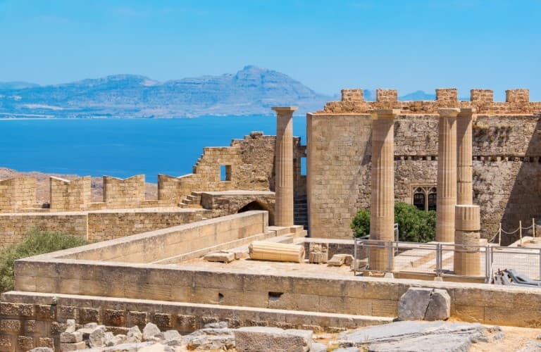 Stunning view of Rhodes Castle surrounded by turquoise sea, green landscapes, and the beautiful natural scenery of Rhodes Island in Greece.