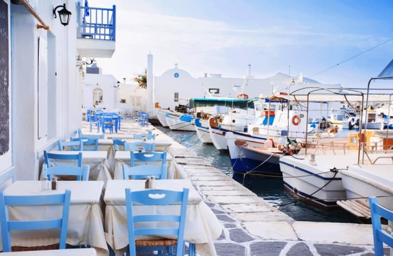 Scenic view of Paros coastline featuring colorful fishing boats, seaside restaurants, and a lively Greek harbor atmosphere in Greece.