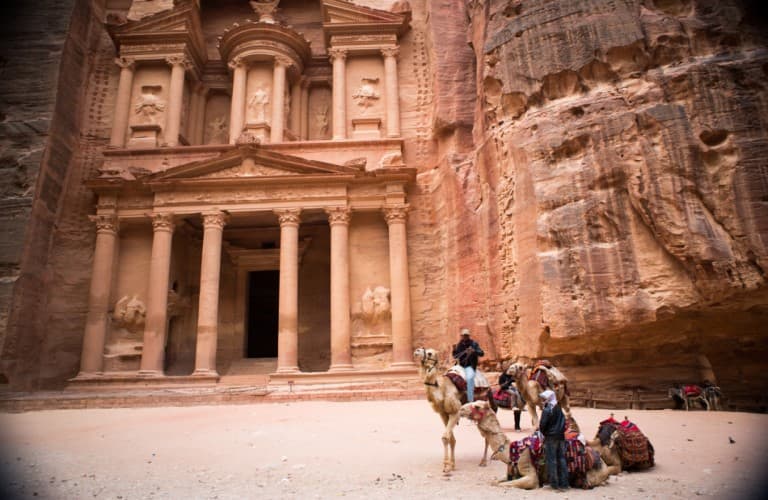 Camel caravan and tourist groups in front of Petra Valley, showcasing Jordan’s iconic sandstone landscape and historic archaeological site.