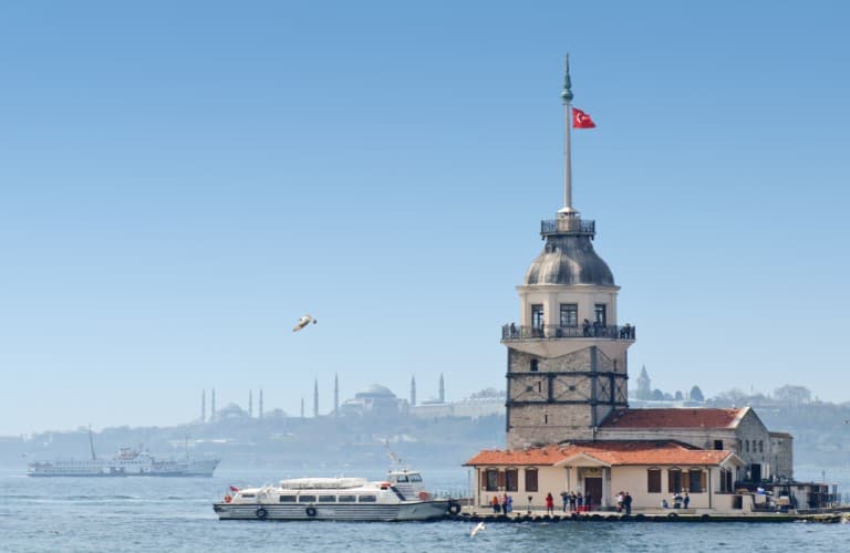 Maiden's Tower stands on the Bosphorus with Topkapi Palace and the Blue Mosque creating Istanbul's iconic historic skyline in the background.